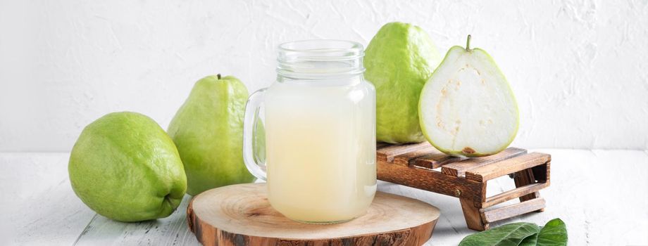 Delicious beautiful guava fruit with fresh juice set isolated on bright white wooden table background, close up.