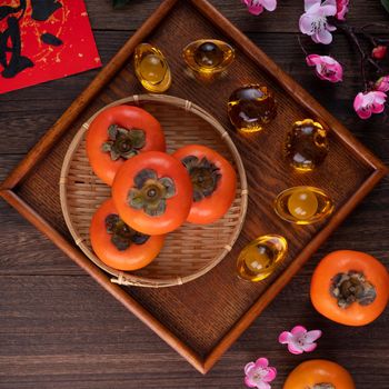 Top view of fresh sweet persimmons kaki with leaves on wooden table background for Chinese lunar new year fruit design concept, the word means blessing is coming.