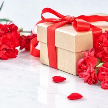 Close up of Mother's Day greeting gift with red flower on modern marble desk, close up, copy space
