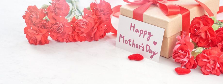 Close up of Mother's Day greeting gift with red flower on modern marble desk, close up, copy space
