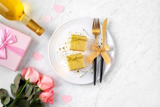 White plate with gift and pink rose flower on marble white table background for Valentine's Day special holiday dating meal concept.