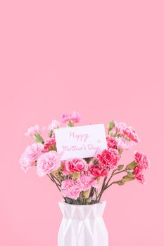 Mother's Day holiday gift design concept, pink carnation flower bouquet with greeting card, isolated on light pink background, copy space.