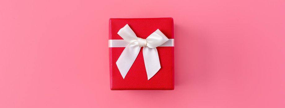 Beautiful gift box wrapped with ribbon bow on pastel pink background.