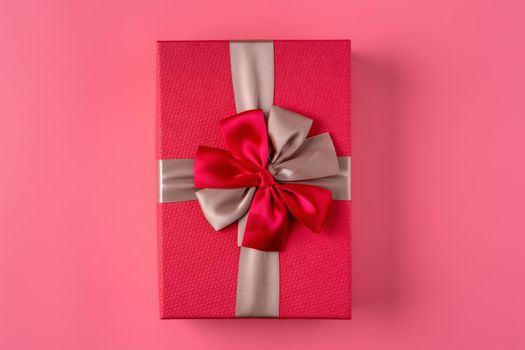 Beautiful gift box wrapped with ribbon bow on pastel pink background.