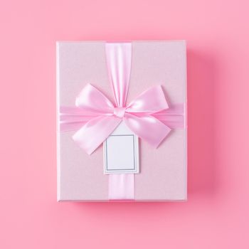 Beautiful gift box wrapped with ribbon bow on pastel pink background.