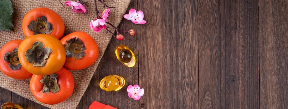 Top view of fresh sweet persimmons kaki with leaves on wooden table background for Chinese lunar new year fruit design concept, the word means blessing is coming.
