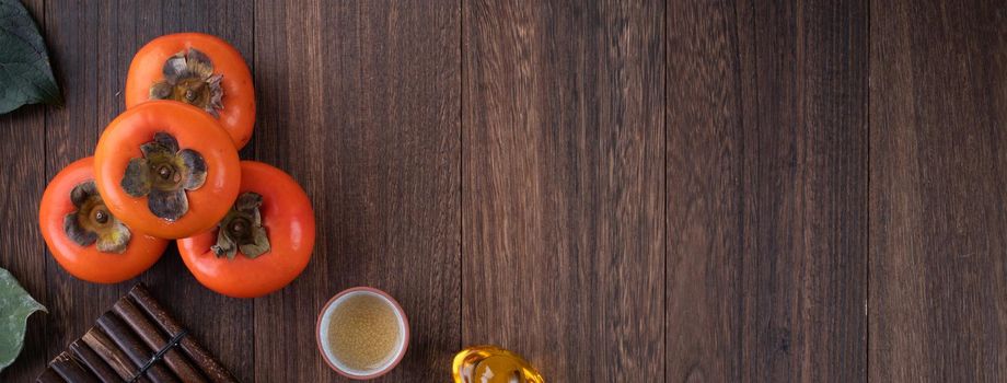 Top view of fresh sweet persimmons kaki with leaves on wooden table background for Chinese lunar new year fruit design concept, the word means blessing is coming.