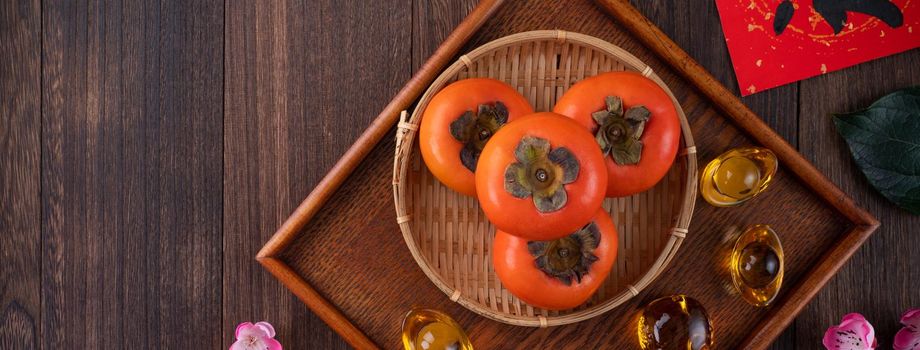 Top view of fresh sweet persimmons kaki with leaves on wooden table background for Chinese lunar new year fruit design concept, the word means blessing is coming.