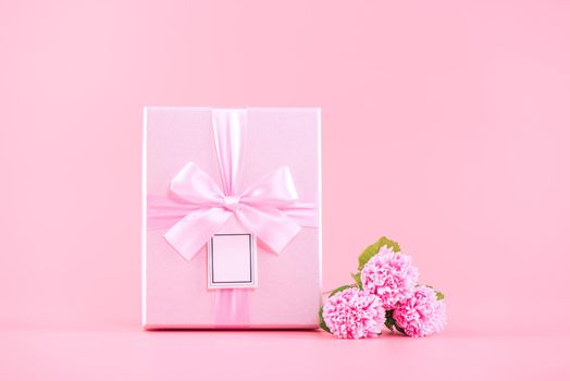 Mother's Day holiday gift design concept, pink carnation flower bouquet with wrapped gift box isolated on pink background, copy space.