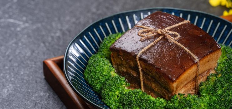 Dong Po Rou (Dongpo pork meat) in a beautiful blue plate with green broccoli vegetable, traditional festive food for Chinese new year cuisine meal, close up.
