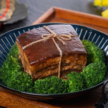 Dong Po Rou (Dongpo pork meat) in a beautiful blue plate with green broccoli vegetable, traditional festive food for Chinese new year cuisine meal, close up.