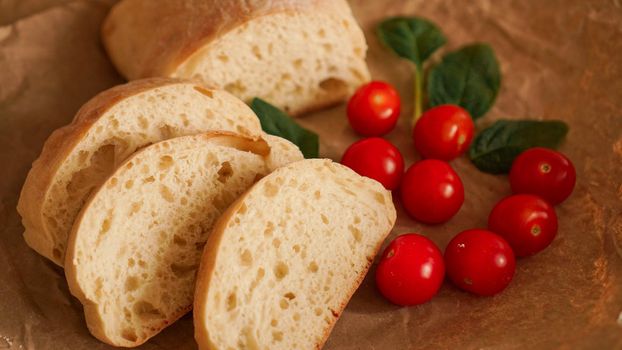 Ciabatta slices and cherry tomatoes on craft paper. Cooking healthy snacks. Ingredients for bruschetta