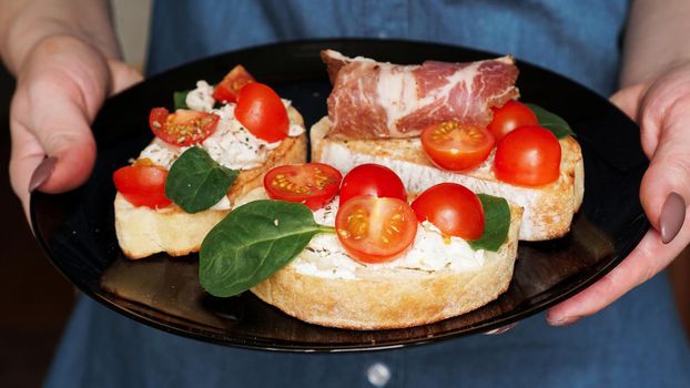 Woman waiter holding a wooden tray with bruschetta with cherry tomatoes in her hand. Delicious italian appetizer