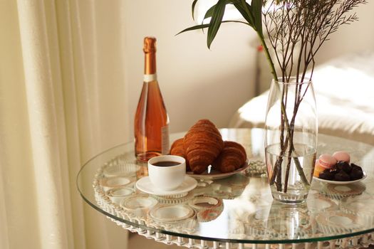 Glass table with a cup of coffee, sweet croissants. On the table is a bottle of wine and glasses. A festive and romantic photo. Morning after da