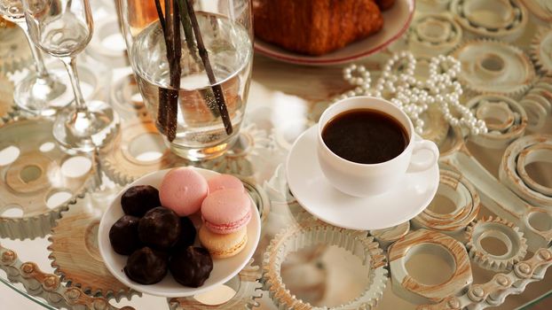 Glass table with a cup of coffee, sweet macaroons. A festive and romantic photo. Morning after date