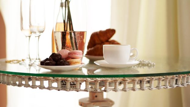 Glass table with a cup of coffee, sweet croissants. On the table is a bottle of wine and glasses. A festive and romantic photo. Morning after da