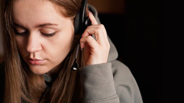 Portrait of a young girl in a hoodie and with a headset. Call center worker. Remote work from home. Brown tones pictures