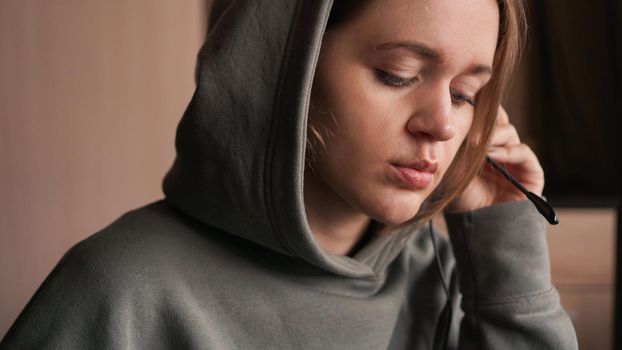 Portrait of a young girl in a hoodie and with a headset. Call center worker. Remote work from home. Brown tones pictures