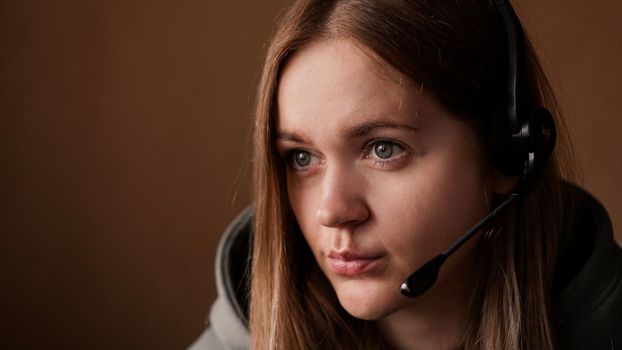 Portrait of a young girl in a hoodie and with a headset. Call center worker. Remote work from home. Brown tones pictures