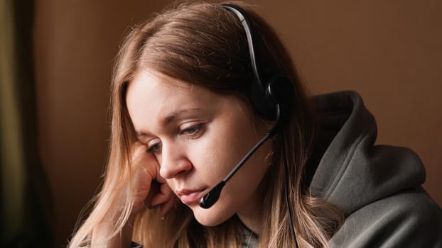 Portrait of a young girl in a hoodie and with a headset. Tired girl streamer or call center worker.