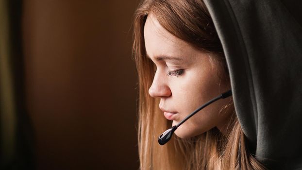 Portrait of a young girl in a hoodie and with a headset. Call center worker. Beautiful girl in the hood. Remote work from home. Brown tones pictures