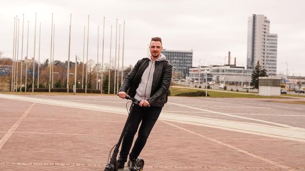 Modern man riding electric scooter in the city. A young man in a black jacket drives around the city on a sunny day.