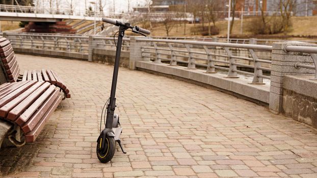 Electric scooter in the park next to the bench. Photos without people. Early spring park