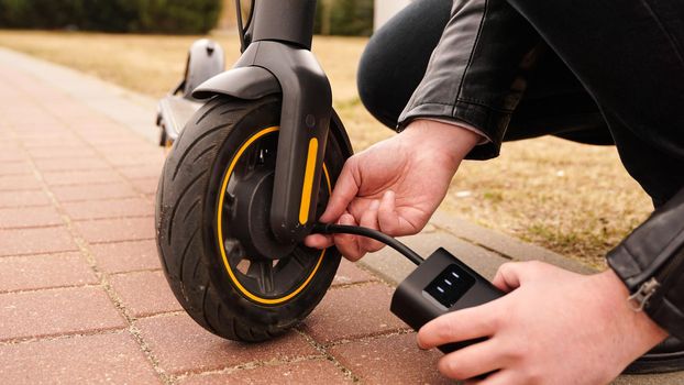 A man pumps air into the wheel of an electric scooter using a special device. Photo outside. A flat tire while driving.