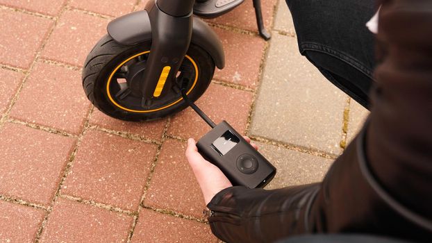 A man pumps air into the wheel of an electric scooter using a special device. Photo outside. A flat tire while driving.