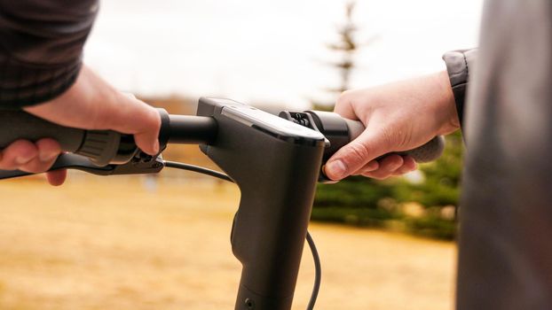 Close-up of male hand pressing speed button on electric scooter. Photo outdoors in the park