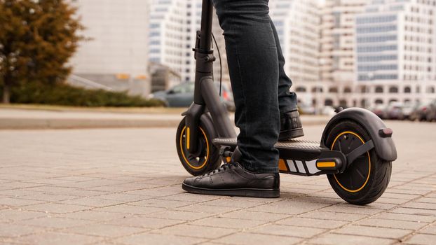 Cropped image of young man riding in the street on electric kick scooter. A man starts to ride a scooter