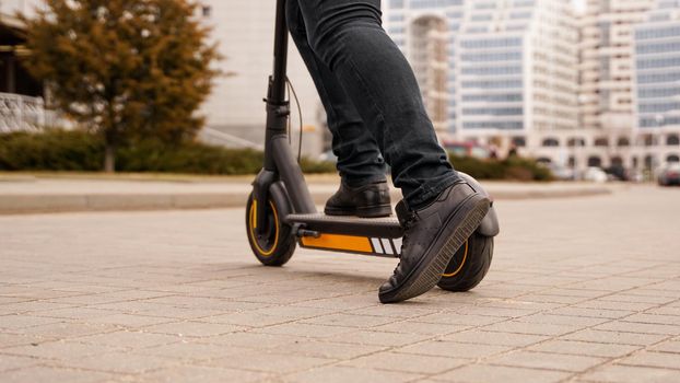 Cropped image of young man riding in the street on electric kick scooter. A man starts to ride a scooter