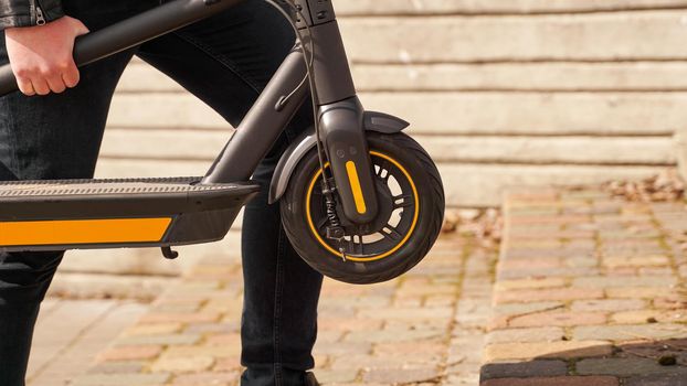 Close up of young men carries electrical kick scooter in hand, environment friendly transport