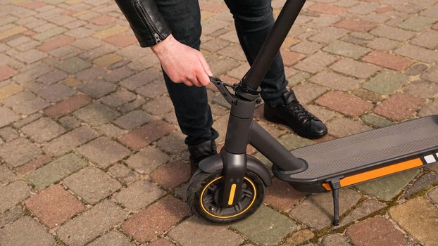 Young man folding an electric scooter in street outdoor. Close up photo