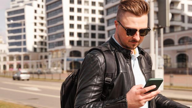 A young man in sunglasses looks at the phone in the city. City navigation and online maps