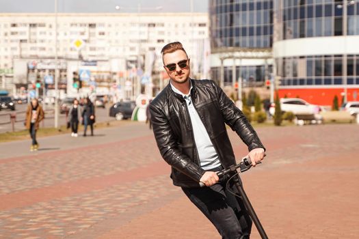 Modern man riding electric scooter in the city. A young man in a black jacket drives around the city on a sunny day.