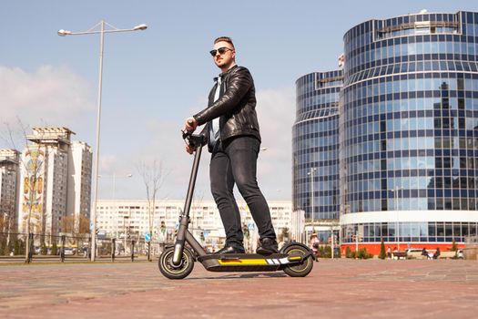 Modern man riding electric scooter in the city. A young man in a black jacket drives around the city on a sunny day.