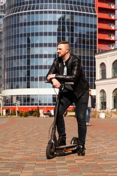 Innovative transport. Glad optimistic guy leaning on electric scooter against the backdrop of a glass building in the city