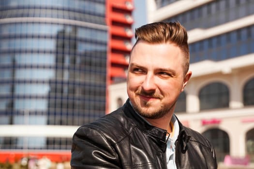 An attractive man wearing black leather jacket against the backdrop of a glass building in the city