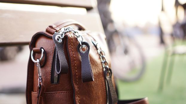 Brown leather bag outside. Blurred summer background. City walk or travel concept