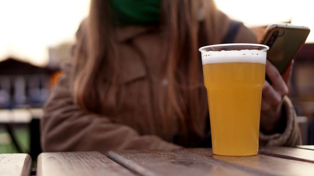 Light beer in a plastic glass. Girl drinking beer at the food court - blurred background