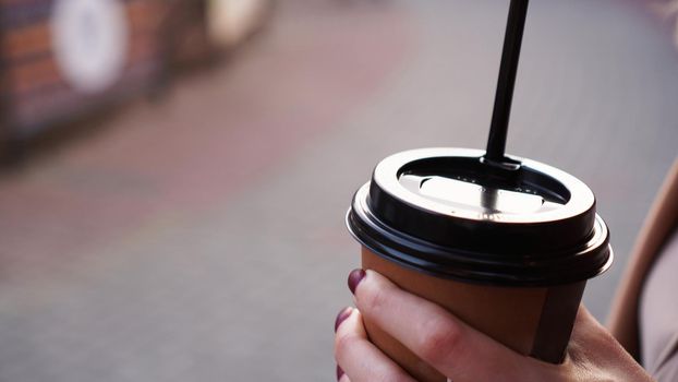 Woman's hand holding a cup of coffee outside against the backdrop of the city sidewalk