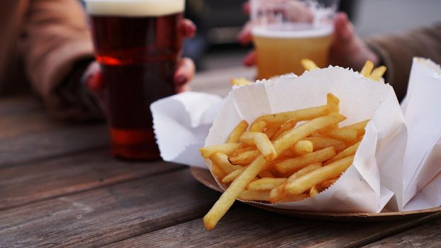 Girlfriends drink beer at the street food festival. Plastic glass of beer in hand. French fries, unhealthy food