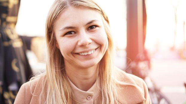 Portrait of a young woman in the city. City food court with street food. Portrait of a smiling blonde. Glare of the sun