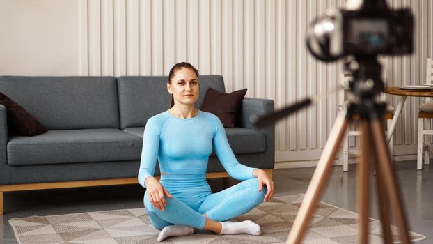 Female blogger recording sports video at home. A woman in a yoga pose is recording video for an online course. Doing sports on your own at home.