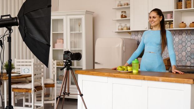 A woman in a tracksuit records a video blog about sports and healthy eating. Professional equipment in the photo studio with kitchen interior