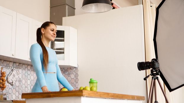 A woman in a tracksuit records a video blog about sports and healthy eating. Professional equipment in the photo studio with kitchen interior