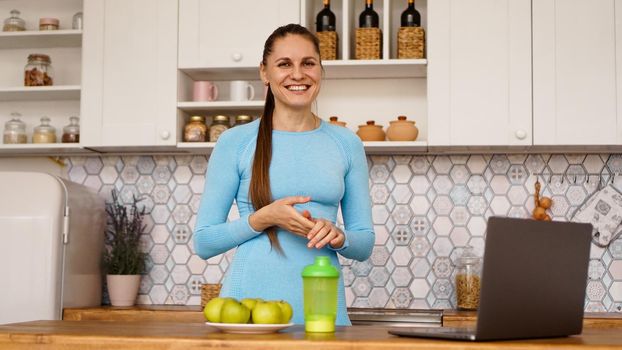 Smiling woman using computer in modern kitchen interior. Cooking and healthy lifestyle concept. A woman is looking at the camera and smiling