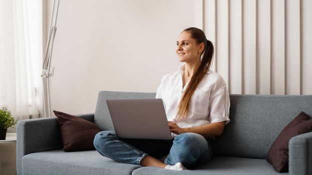 Woman working on laptop from home or student studying from home or freelancer. Modern business woman in a white shirt and jeans.