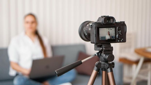 Woman blogger recording video indoors, selective focus on camera display. Space for text